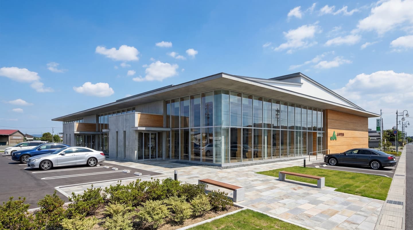 晴天の下に建つモダンなJA（農業協同組合）の店舗外観パース。大きなガラス張りの窓、木目調のサイディング、打ち放しコンクリートを組み合わせた平屋の現代建築。手前には緑豊かな植栽とベンチがあり、舗装された駐車場には数台の車が停まっている。生成AIによって作成されたリアルな建築イメージ。